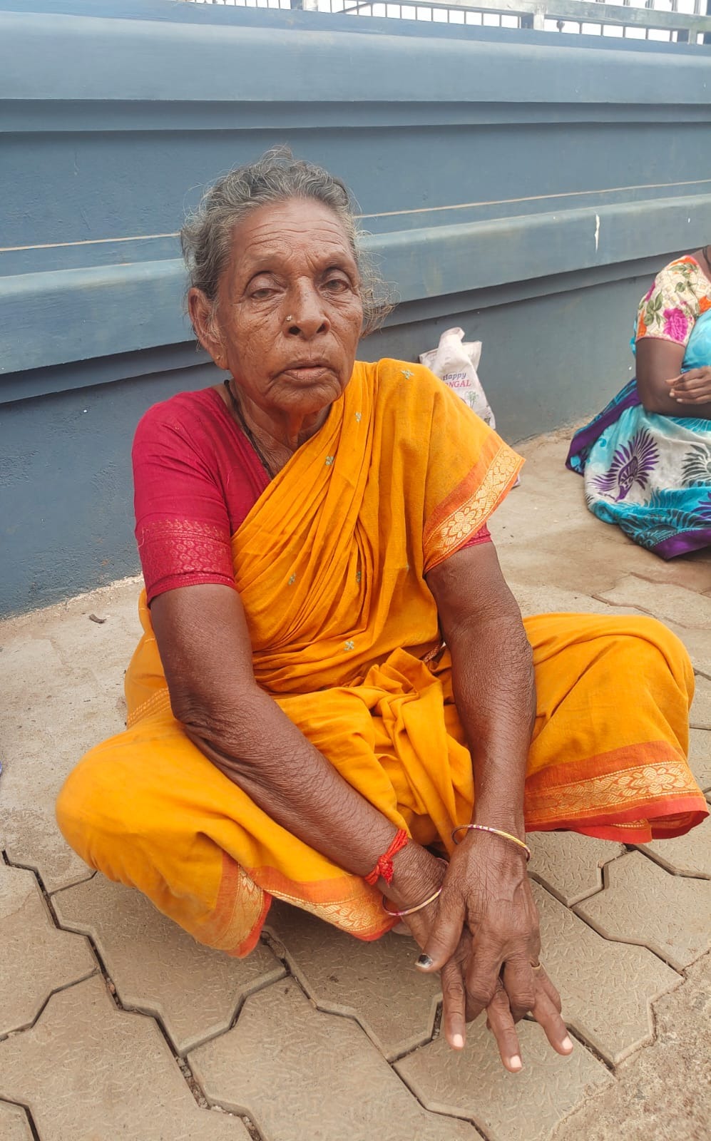 Pattu paati sitting alone on a footpath in a yellow saree, weak and unwell before her rescue